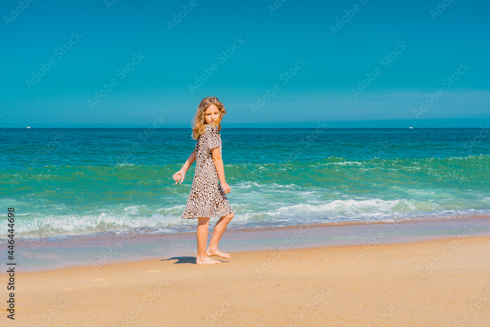 Young beautiful girl in beige dress running on the the sandy beach near the waves. High quality photo