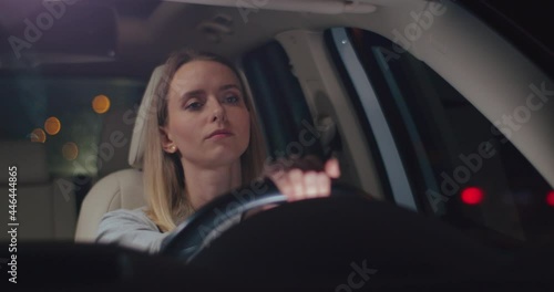 Tired young caucasian woman is driving a car on a road looking around. Road from work. Car's interior. Front view. Close up.