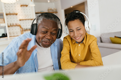 Happy African grandfather and grandson sitting together at home and listening to good music. Granddad helping his grandson to explore music on the internet.