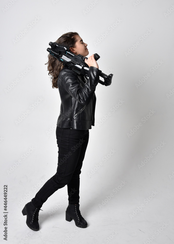 Full length portrait of young woman with natural brown hair, wearing black leather scifi outfit with jacket, standing pose on light studio background. Full length portrait of young woman with natural brown hair, wearing black leather scifi outfit with jacket, standing pose on light studio background.