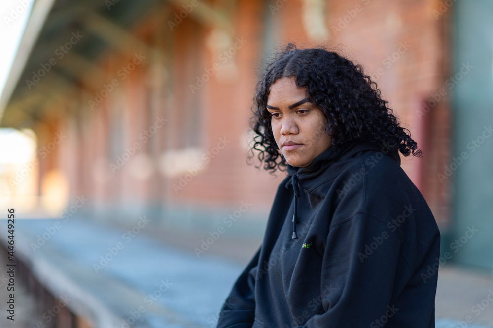 Young aboriginal woman wearing black hoody against blurred background of old station platform Young aboriginal woman wearing black hoody against blurred background of old station platform