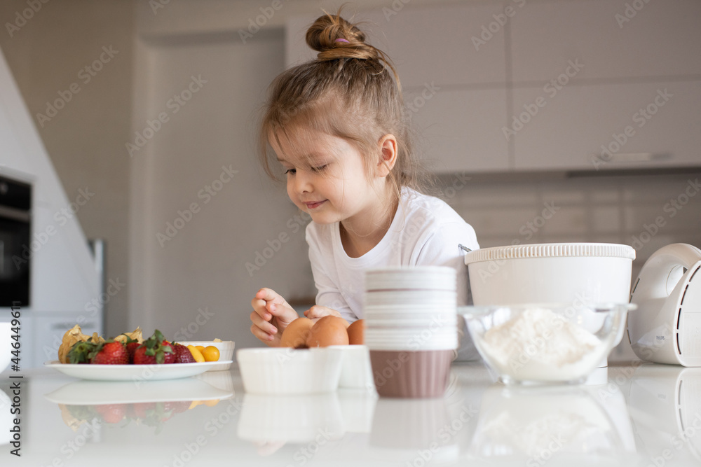 Smiling baby girl 3-4 year old making dough in white bowl for cake on kitchen table at home close up. Kid cook pastry with ingredients. Childhood. Smiling baby girl 3-4 year old making dough in white bowl for cake on kitchen table at home close up. Kid cook pastry with ingredients. Childhood.