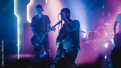 Rock Band with Guitarists and Drummer Performing at a Concert in a Night Club. Lead Singer Singing into Microphone. Live Music Party in Front of Bright Colorful Strobing Lights on Stage.  © Gorodenkoff