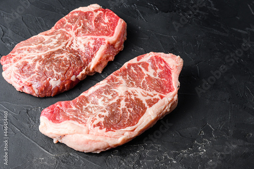 Organic top blade steak cuts, on black textured background side view with space for text.