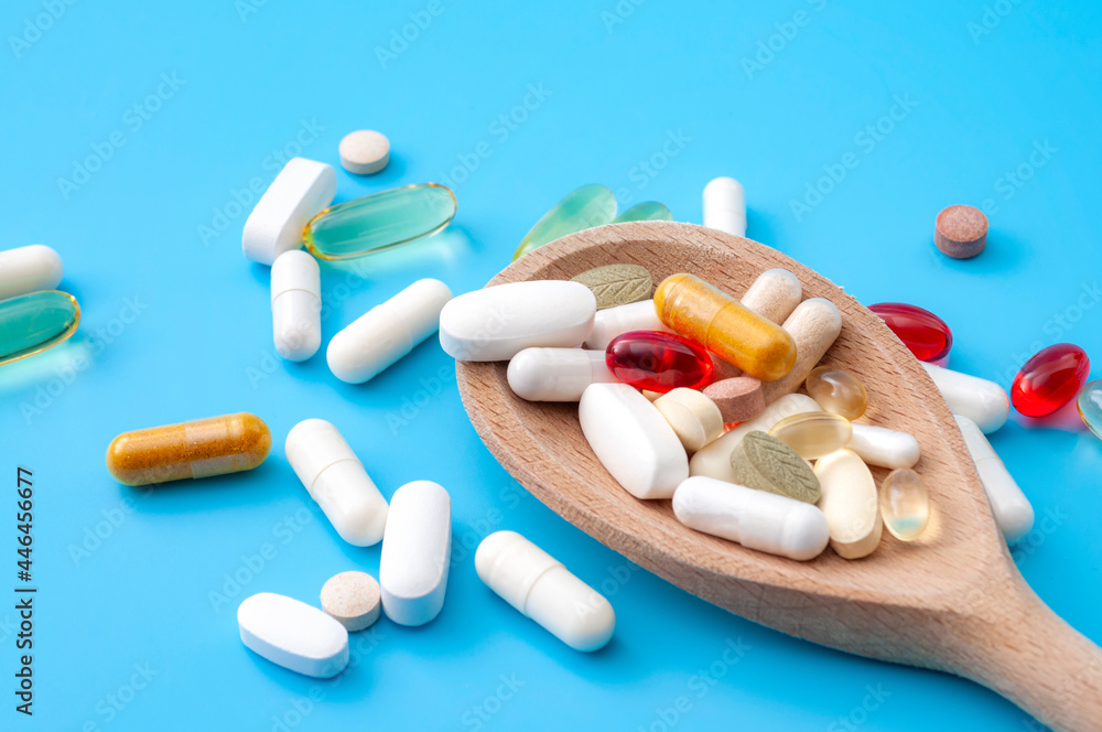 Wellness, herbal supplement and wellbeing concept with mix selection of supplements and vitamins in a wood spoon isolated on blue background