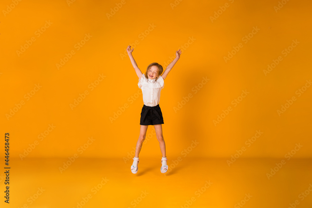 a little blonde girl in a school uniform jumps on a yellow background with a place for text