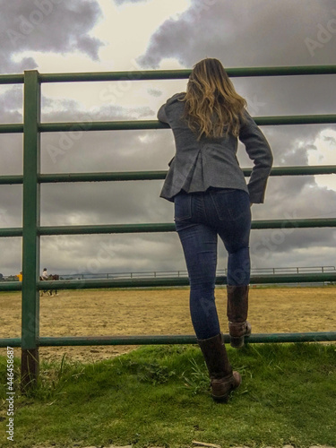 Mujer observando sobre la cerca a un jinete sobre su caballo.