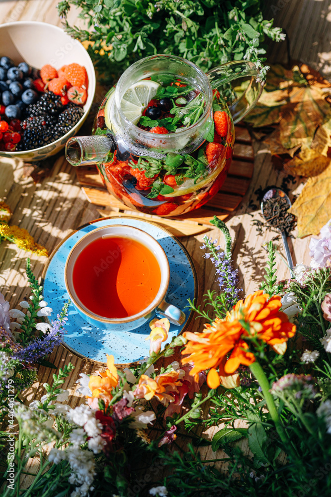 natural aromatic fruit tea in a transparent teapot and in a cup among berries and flowers. warming aromatic tea with a deep aroma of berries and wildflowers.