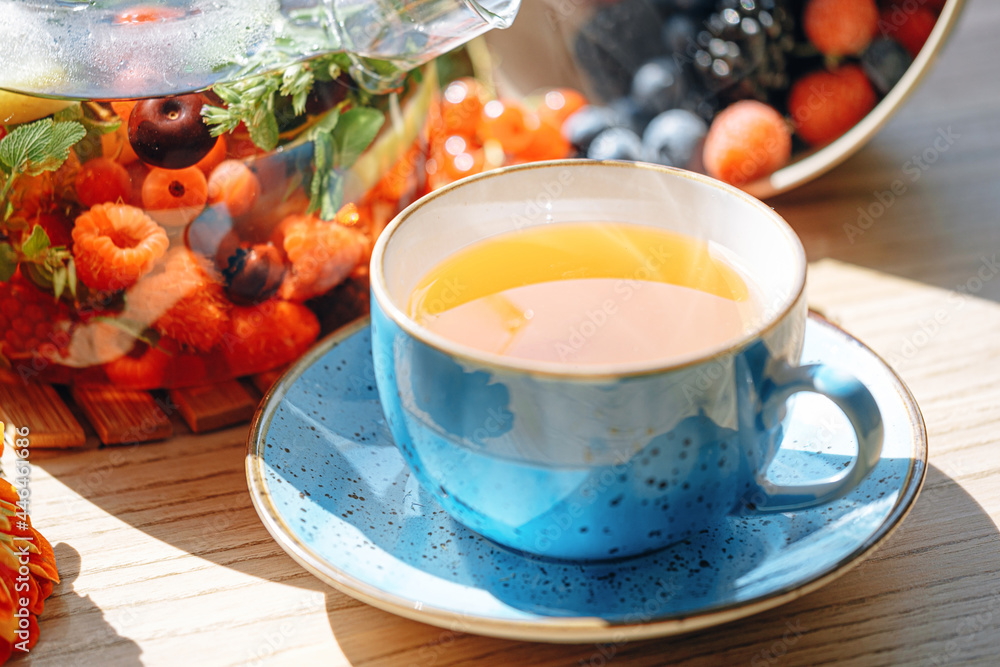 natural aromatic fruit tea in a transparent teapot and in a cup among berries and flowers. warming aromatic tea with a deep aroma of berries and wildflowers. natural aromatic fruit tea in a transparent teapot and in a cup among berries and flowers. warming aromatic tea with a deep aroma of berries and wildflowers.