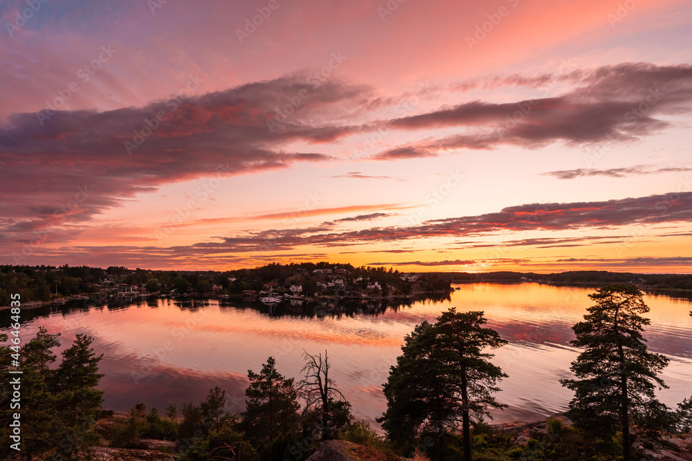 Amazing Beautiful sunset on the Baltic Sea. Bright golden orange pink purple tones of the sunset sky. Rocky Islands of Stockholm archipelago covered with evergreens. Villas on the other coast shore.