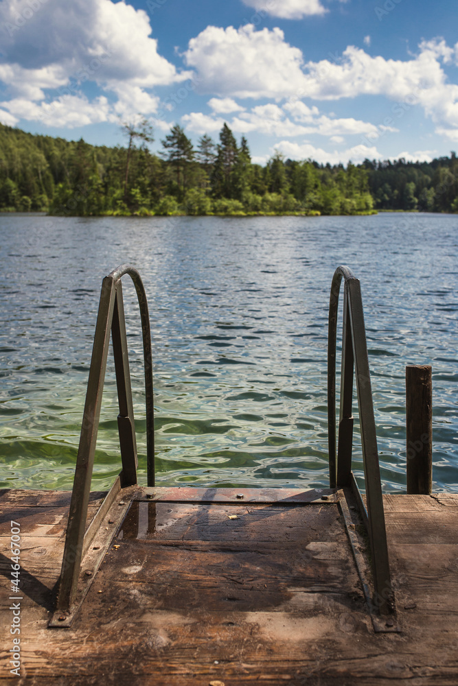 Metal handrails and ladder to descend into the water on a wooden pier of a forest lake - a place for swimming