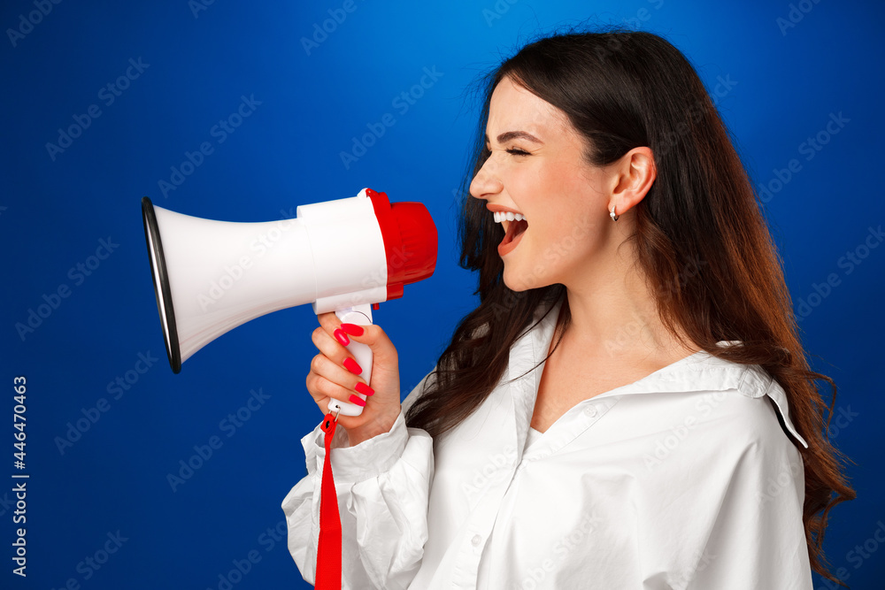 Young brunette businesswoman holding a megaphone against blue background Young brunette businesswoman holding a megaphone against blue background