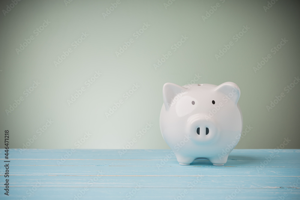 The white piggy bank on blue wooden table green background with copy space. Concept money savings everyone to save, financial, banking, accounting, business, and investing. The white piggy bank on blue wooden table green background with copy space. Concept money savings everyone to save, financial, banking, accounting, business, and investing.
