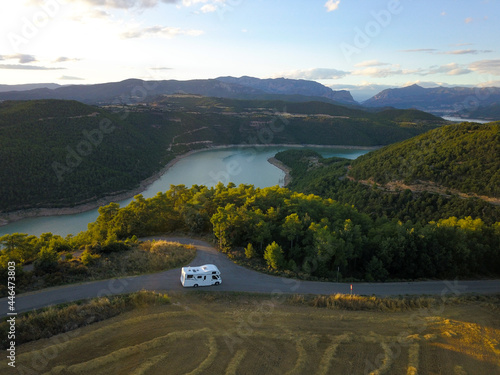 Awesome aerial drone view of an incredible lake road with a van driving it at sunset.