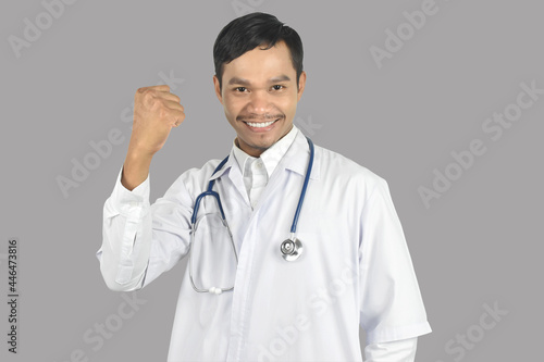Young doctor smiling with stethoscope showing yes of success gesture on grey background. copy space.