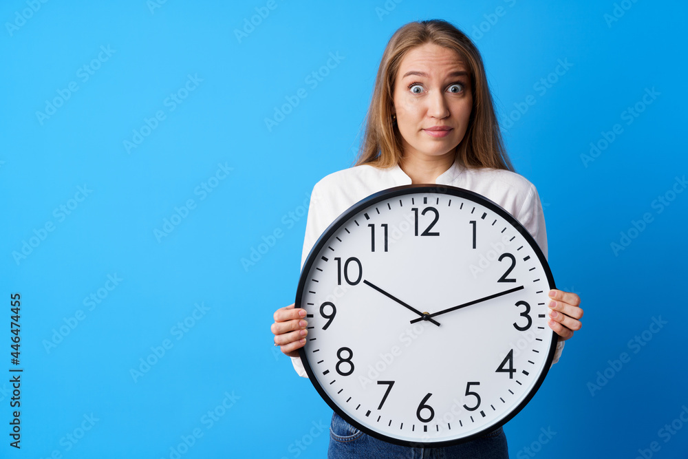 Attractive young woman holding big wall clock against blue background Attractive young woman holding big wall clock against blue background