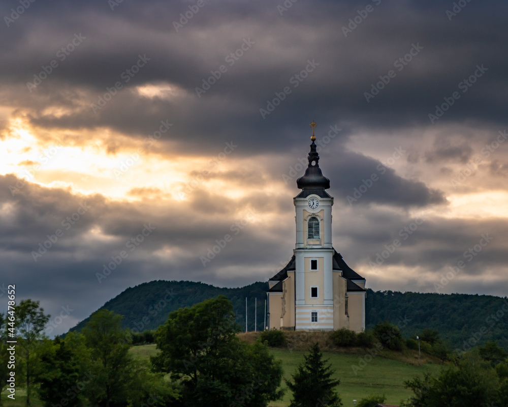 Der Sonnenuntergang zwischen den Gewitterwolken vor der Kulisse der Kirche