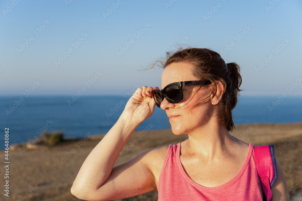 Beautiful Caucasian woman putting on her sunglasses at sunset in a park near the sea. Beautiful Caucasian woman putting on her sunglasses at sunset in a park near the sea.