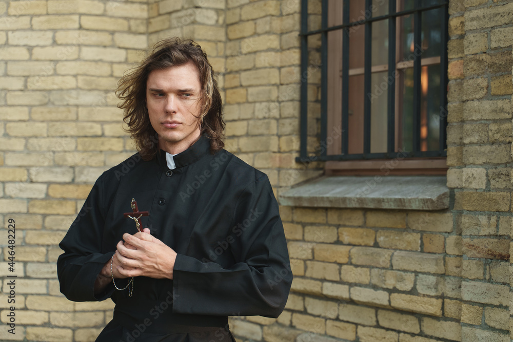 Christian priest with cross standing by the church.