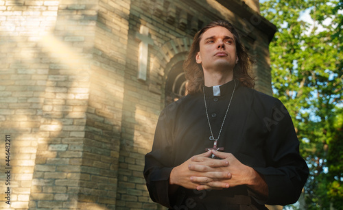 Christian priest with cross standing by the church.