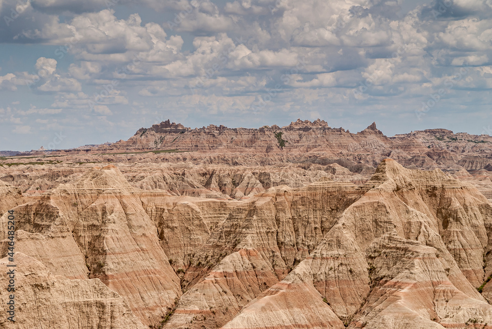 Badlands National Park, SD, USA - June 1, 2008: Wide landscape filled by beige mountains and heavy blue cloudscape. Colored lines run horizontally through entire range.