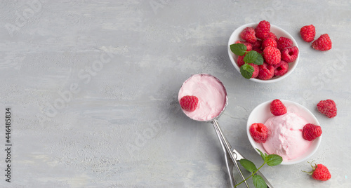 A scoop of homemade raspberry ice cream with fresh raspberries and mint in a white cup on a light background. Delicious and romantic dessert. Top view. Copy space