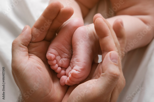 Father holding Baby Feet in Hands. Legs Newborn in male parents Hand. Small children's Feet in the Father's Palm. Close-up. Little Toes of Child and Man Hands of Happy Parent. Father's Day Holiday