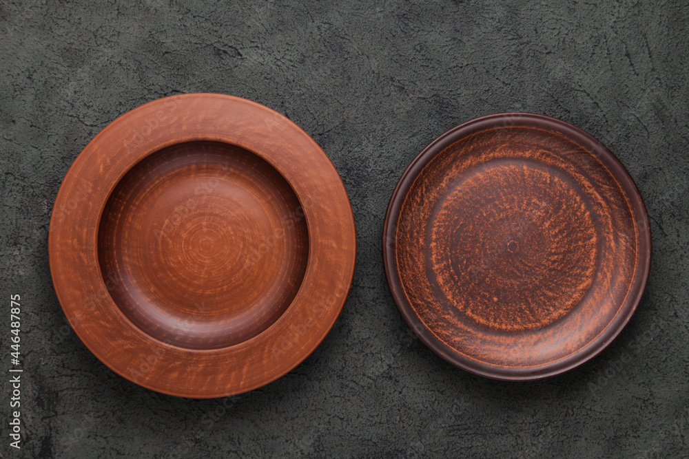 Two Rustic Plates on gray background. Empty brown clay plate on black stone table. Top view with copy space. Rustic dishes Two Rustic Plates on gray background. Empty brown clay plate on black stone table. Top view with copy space. Rustic dishes