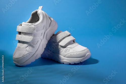 Foto white children's running shoes with velcro fasteners for easy shoeing on a purple background with fern shadows