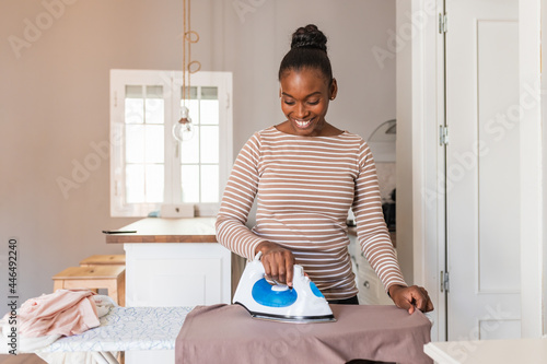 Black woman ironing clothes in kitchen at home