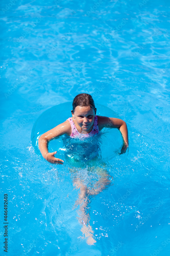 a happy girl swims in a swimming pool in an inflatable circle for safety on the water, with copy space. 