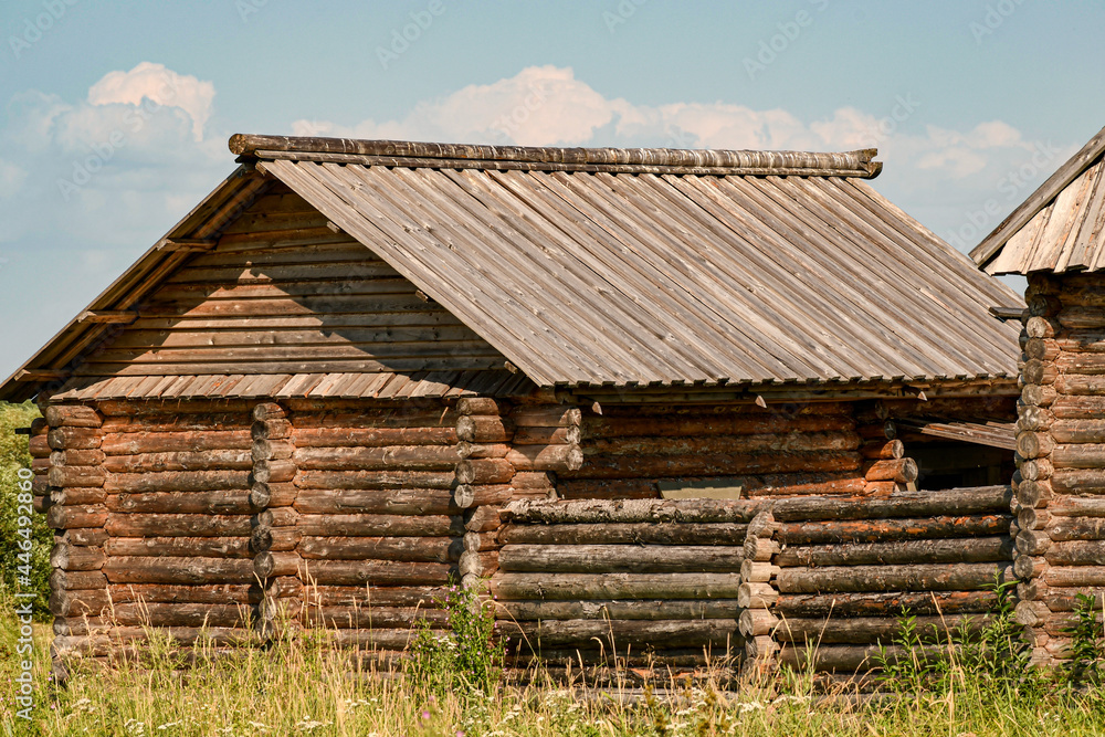 An old wooden Russian shed with a log fence. Old darkened boards. Side view. An old wooden Russian shed with a log fence. Old darkened boards. Side view.
