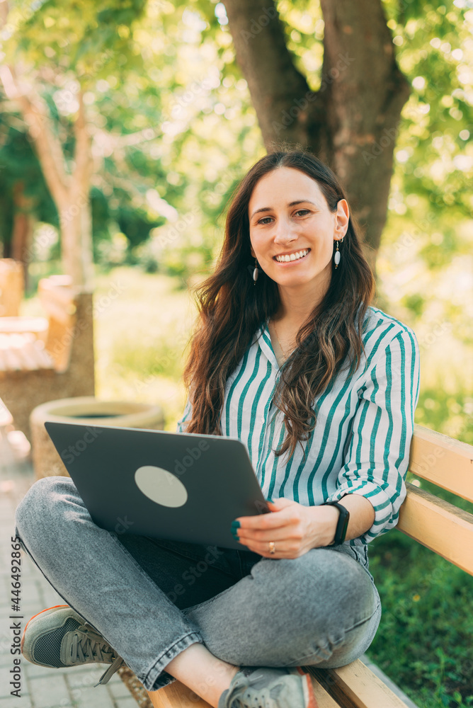 Obraz premium The girl on the bench uses a laptop, freelancer working remotely