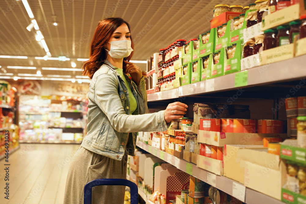 Pretty woman choosing groceries at supermarket. Female consumer purchasing goods at mall, walking among shelves. Girl with mask shopping of food