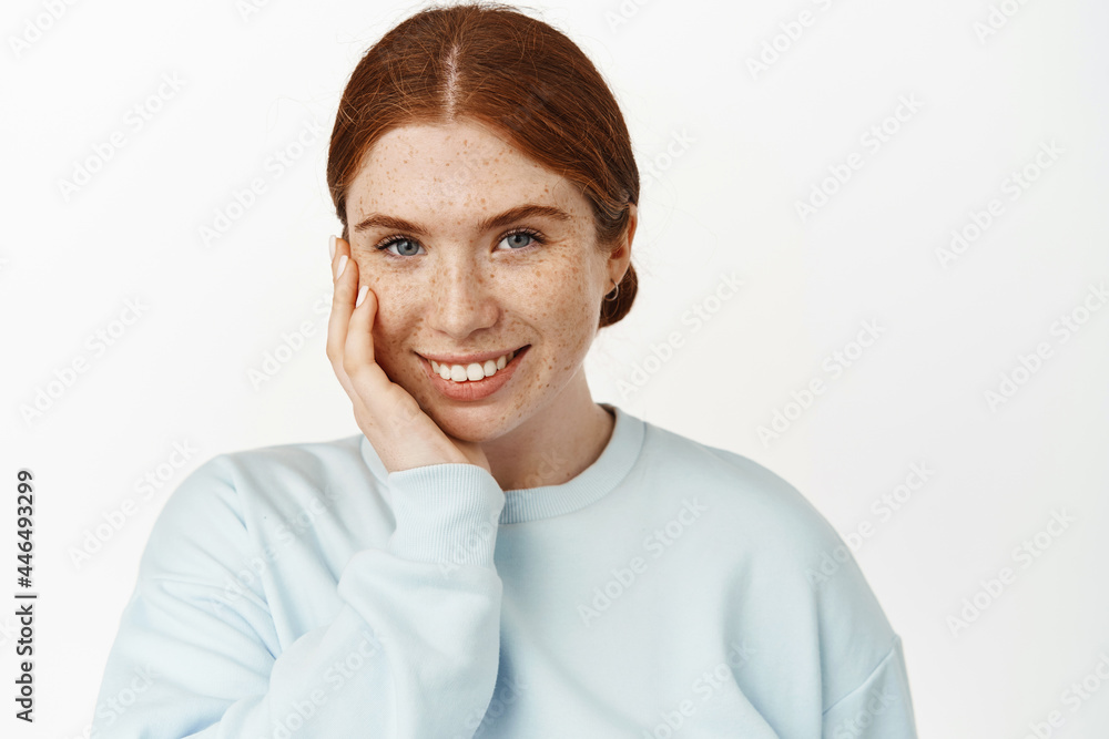 Women beauty. Tender and feminine redhead girl, smiling white teeth, touching pale facial skin with freckles, natural look without make up, clean face, white background Women beauty. Tender and feminine redhead girl, smiling white teeth, touching pale facial skin with freckles, natural look without make up, clean face, white background