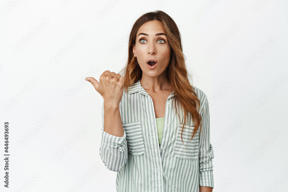 Portrait of surprised adult woman gasp in wow, pointing left with dropped jaw, impressed excited face, checking out advertisement, big promo offer, standing over white background Portrait of surprised adult woman gasp in wow, pointing left with dropped jaw, impressed excited face, checking out advertisement, big promo offer, standing over white background