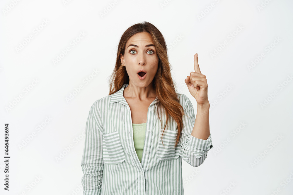 Image of surprised middle aged woman, businesswoman pointing finger up with WOW face, checking out smth awesome, impressive big sale, standing over white background Image of surprised middle aged woman, businesswoman pointing finger up with WOW face, checking out smth awesome, impressive big sale, standing over white background