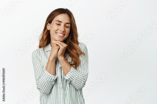 Dreamy brunette woman smiling, close eyes and dreaming, imaging smth beautiful, picturing perfect moment, standing hopeful against white background