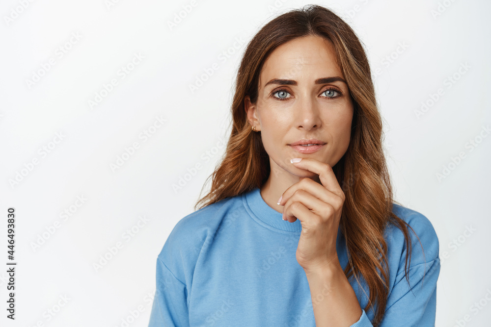 Close up of thoughtful adult woman with smiling confident look, touch chin, thinking, looking at camera with ponder face, making decision, choosing, standing over white background Close up of thoughtful adult woman with smiling confident look, touch chin, thinking, looking at camera with ponder face, making decision, choosing, standing over white background