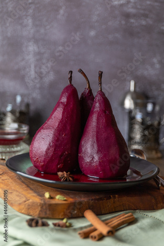 Three pears in red wine on a ceramic plate and concrete wall background.
