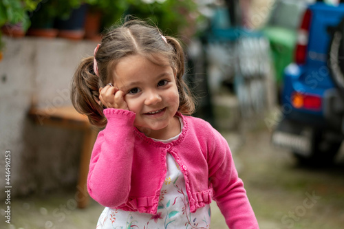Niña con vestido de flore y chaqueta rosa jugando jovial con un peluche de perrito.