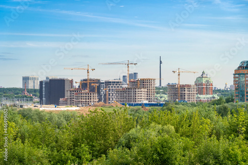 Panoramic view of construction cranes and unfinished residential buildings against clear blue sky. Housing construction, apartment block with scaffolding