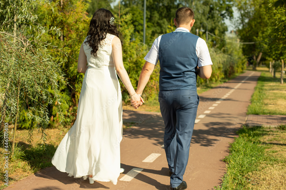 The newlyweds walk along the park path holding hands. The newlyweds walk along the park path holding hands.