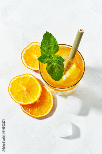 Flat lay of glass of summer trendy sparkling lemonade with orange, mint, ice cubes with bamboo straw, garnished with slices orange on white background.