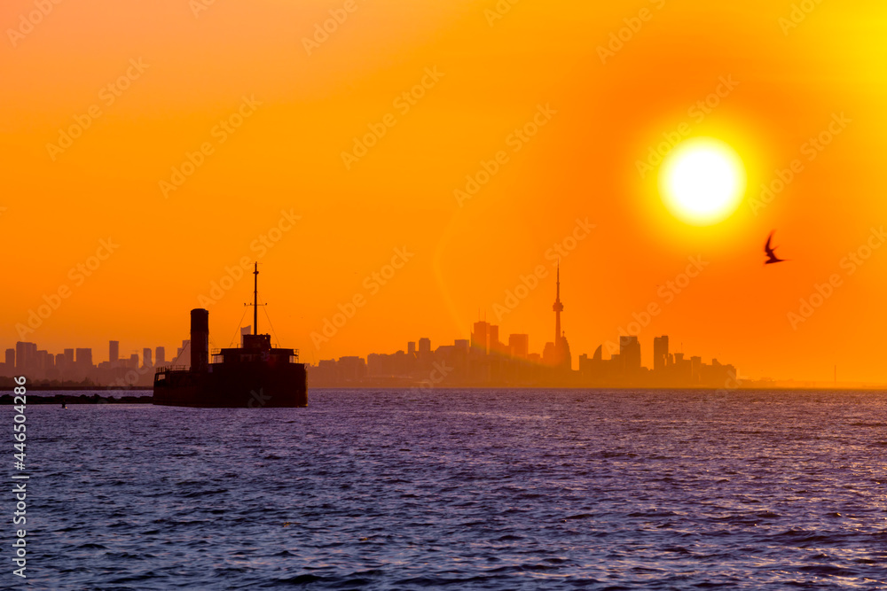 Morning time city landscape over water. Toronto city view. Sunrise, Ontario lake ,  orange sky and sun disc. Big ship in harbor
