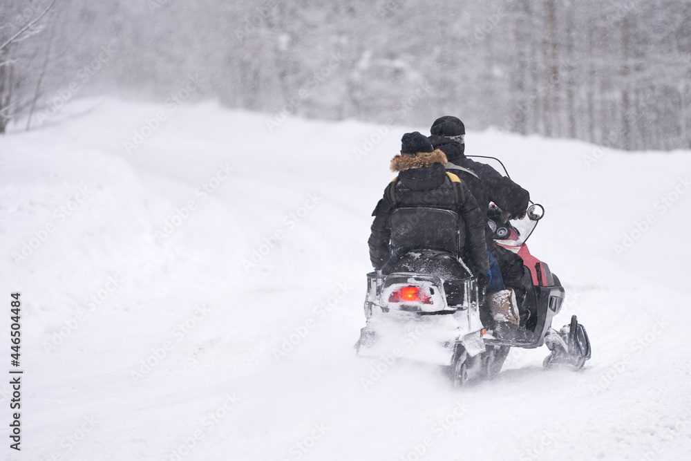 Two men are racing on a snowmobile through snowdrifts in the forest. Snow is falling. Selective focus. Copy space.