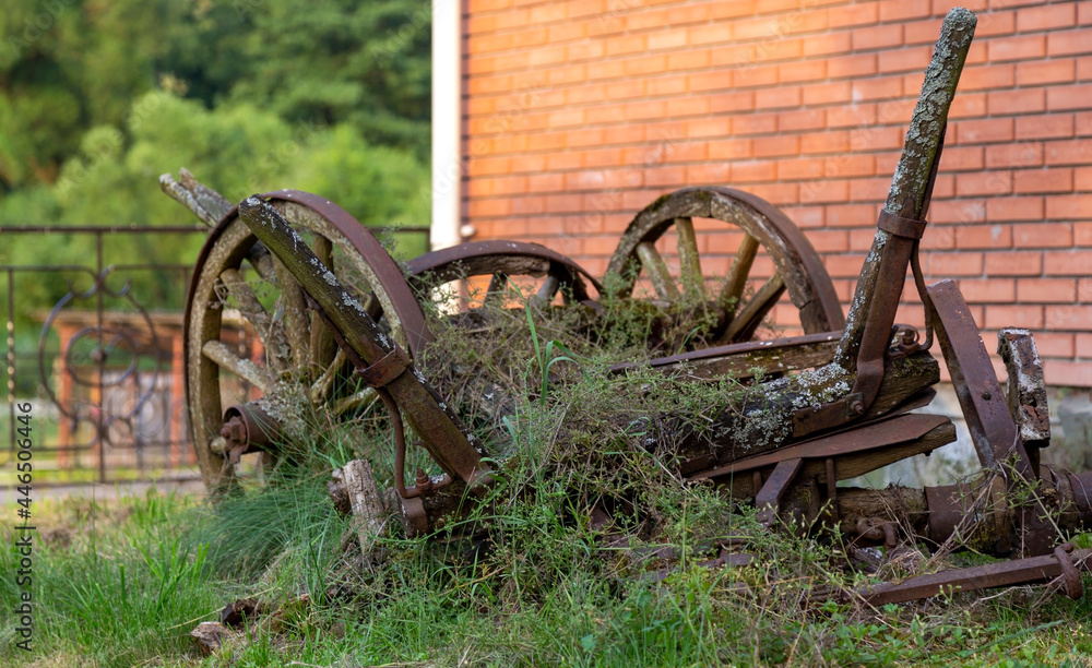 Against the background of a brick house an old broken wooden cart, with broken wheels made of wood Against the background of a brick house an old broken wooden cart, with broken wheels made of wood