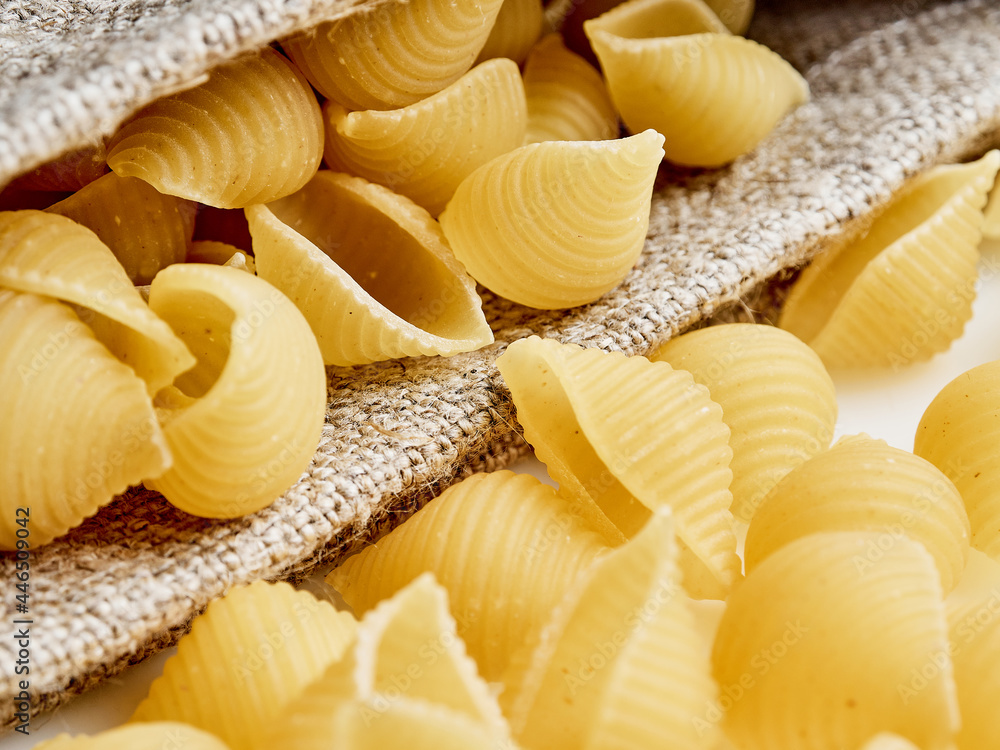 Side view to the raw shell pasta inside sackcloth pouch on the table. Side view to the raw shell pasta inside sackcloth pouch on the table.