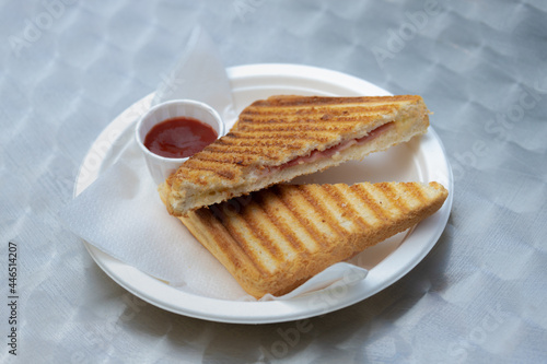 Toasted ham and cheese sandwich in white plastic plate served with tomato ketchup sauce on the side, The tosti in Netherlands or croque-monsieur is a hot sandwich made with ham and cheese. photo