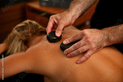 Masseur placing therapeutic hot stones on woman's back. Ayurvedic hot stone massage in modern spa salon. Body care concept
